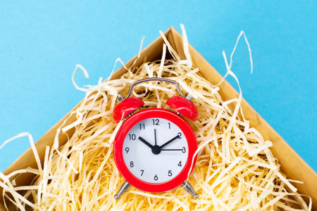 red round analog alarm clock in a box on a blue. time 10:10.
