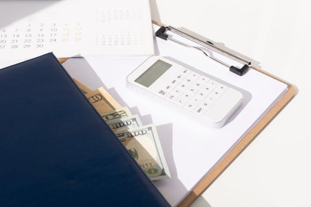 White calculator, calendar and dollars on the office desk. The concept of planning
