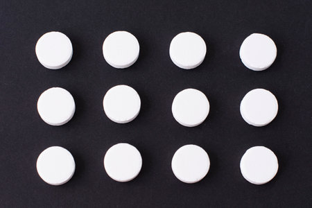 Round white medical pills arranged in square order on a black background. Pill splitting.の写真素材