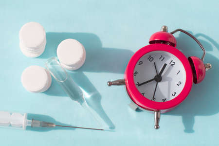 Pills, syringe and red alarm clock on blue background. Medical and health concept in minimal style.の写真素材