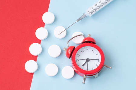 Pills, syringe and red alarm clock on colorful background. Medical and health concept in minimal style.の写真素材