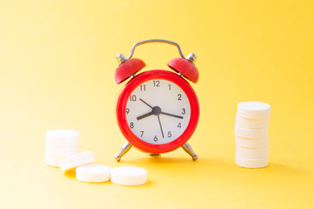 Pills, tablets and red alarm clock on yellow background. Medical and health concept in minimal style.の写真素材