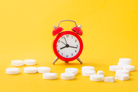 Pills, tablets and red alarm clock on yellow background. Medical and health concept in minimal style.の写真素材