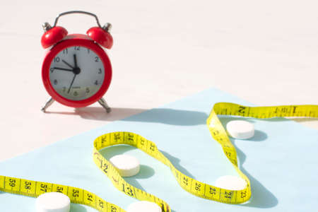 Diet concept.Weight loss pills, red alarm clock and measuring tape. Slim by pills, dangerous for health.の写真素材