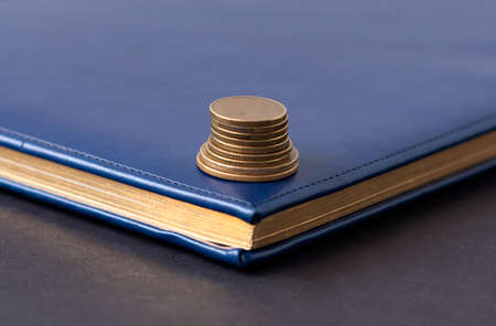 blue diary and stack of coins on a black background. Planning and business conceptの写真素材