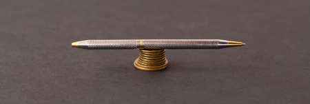 Silver pen on a stack of coins on a black background.の写真素材