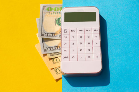 dollar bills and a white calculator on a yellow and blue background. Business concept.