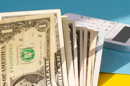 dollar bills and a white calculator on a yellow and blue background. Business concept.の写真素材