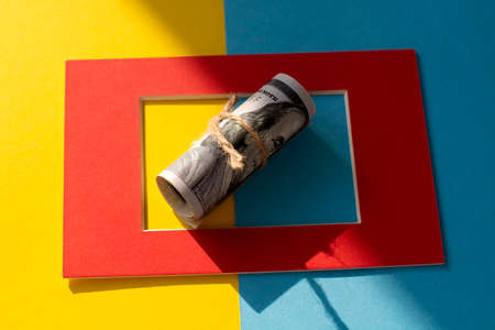 Twisted bundle 100 dollar bills on a yellow and blue background in a red frame. Business conceptの写真素材