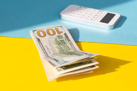 dollar bills and a white calculator on a yellow and blue background. Business concept.の写真素材