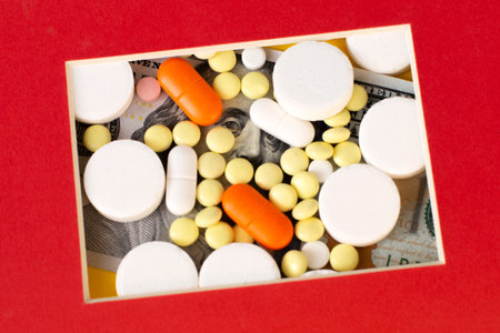 Hundred dollar bill covered with colorful medical pills. Money, healthcare, drug trafficking concept.の写真素材