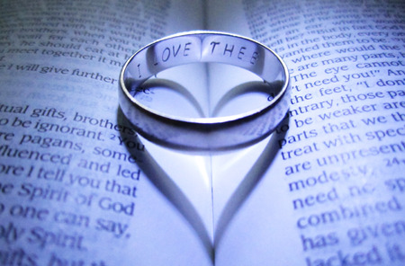 Engraved wedding band making heart shadow on open Bible