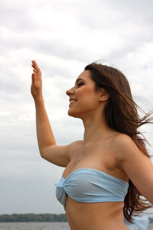 Beautiful smiling girl, brunette with long hair, waves a hand against the skyの写真素材