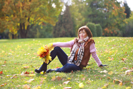 Young woman sitting on the lawn in a park in autumnの写真素材