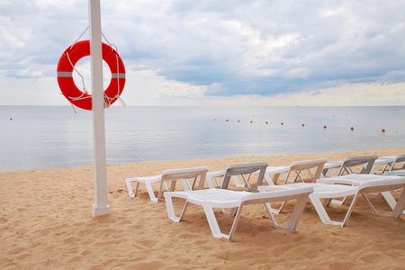 Life ring hanging on a pillar and sun beds on the beach against the sea