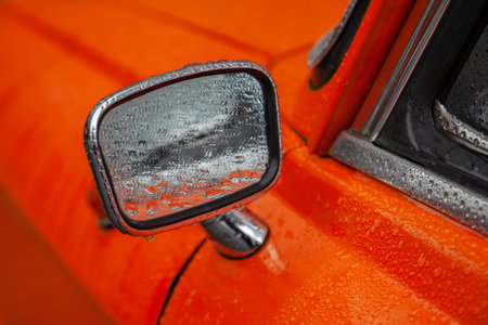 Rear view mirror of an orange retro car in the rain closeupの写真素材