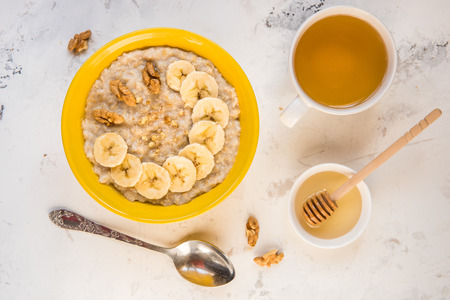 Oatmeal with banana and honey. Porridge in a yellow bowl top view.の写真素材
