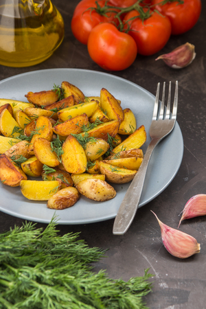 Fried baby potatoes, green, tomatoes and garlic on a dark background.の写真素材
