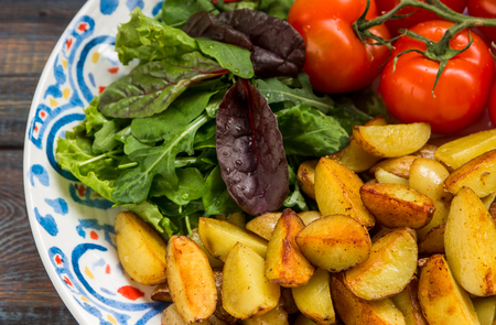 Fried baby potatoes, green salad and fresh tomatoes on a big plate in rustic style.の写真素材