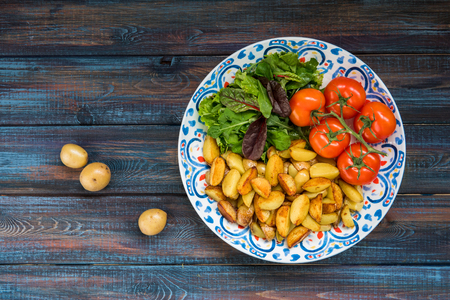 Fried baby potatoes, green salad and fresh tomatoes on a big plate in rustic style.の写真素材
