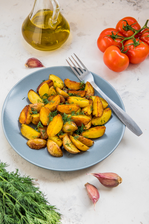 Fried potatoes in a plate. Baby potatoes, green, tomatoes and garlic on the table.の写真素材