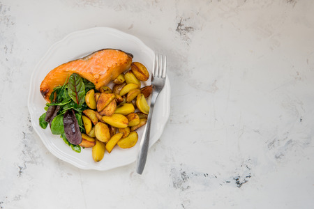 Fried potatoes with fish and green salad on a white plate.の写真素材