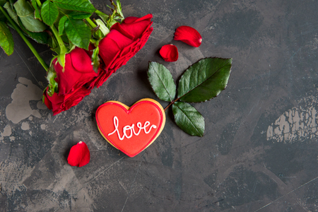 Red roses and cookie shaped heart with text Love, dark background copy space.の写真素材