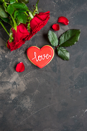 Red roses and cookie shaped heart with text Love, dark background copy space.の写真素材