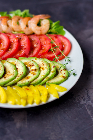 Avocado, tomato, pepper and shrimps on a plate lined with rows. Avocado salad on a dark background.の写真素材