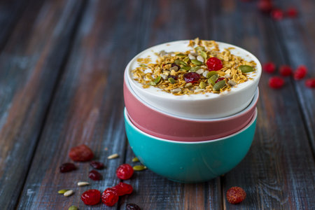 Granola with yoghurt, dried berries and pumpkin seeds on a dark wood table
