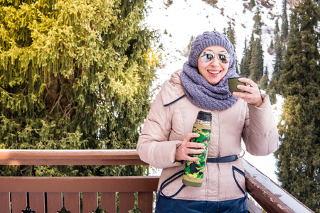 Elderly woman drinks tea from a thermos in the open air.の写真素材