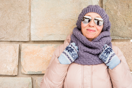 An elderly woman in winter clothes is standing near the wall.の写真素材
