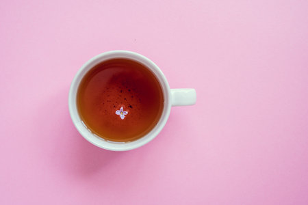 Cup of tea with lilac flower. Pink background