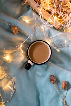 Coffee cup and garland on a bed. Atmospheric swedish hygge style. Cozy winter or autumn conceptの写真素材