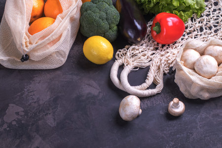 Fresh fruits and vegetables in eco cotton bags on dark background