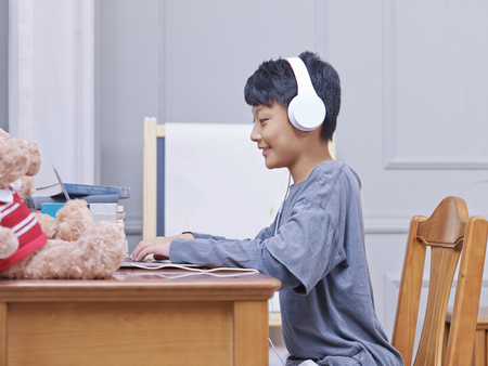 Chinese boy smiling, wearing headphones during online learningの写真素材