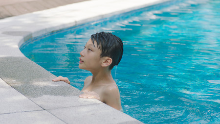 portrait of Asian teenage boy swimming outdoors in blue pool in summerのeditorial素材