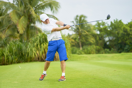 Asian man swinging club in golf course in summerの写真素材