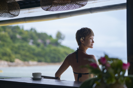 rear view of young Asian beauty sitting, relaxing at beach bar in vacationの写真素材