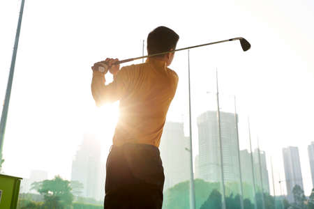 rear view of Asian man practicing golf swing on driving rangeの写真素材