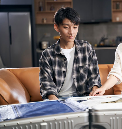Asian kid and parents sitting in living room smiling talking to each other when packing suitcase preparing for travelの写真素材
