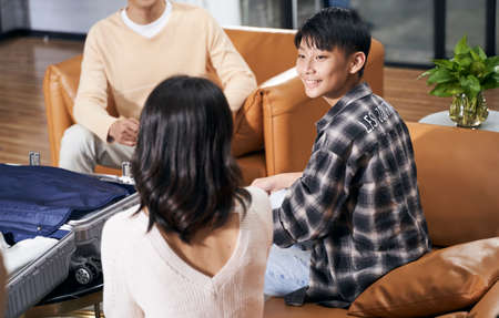 Asian kid and parents sitting in living room smiling talking to each other when packing suitcase preparing for travelの写真素材