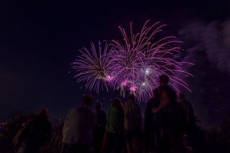 Beautiful firework scene with people as silhouttes watching at the colorful violett rockets at the night.の写真素材