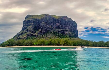 A driving speed boat in front of the popular Le Morne Brabant mountain of the african dream island Mauritius.の写真素材