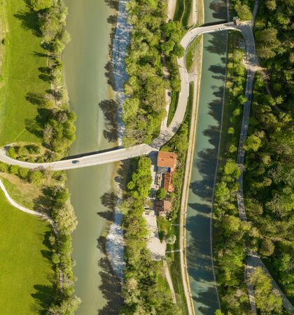 Top view from a drone at a driving car at a bridge over a river with a neaby forest and a houseの写真素材