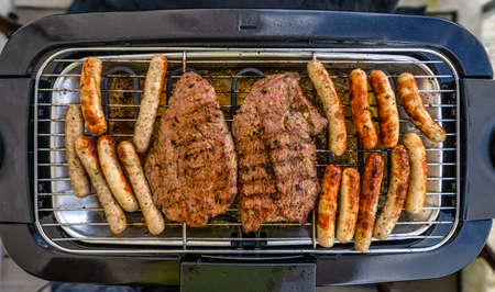 Top view at a bbq grill with meat of beef and little sausages called in germen Nuernberger, ready to eat in tasty condition.の写真素材