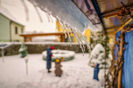 Icicles hanging from house roof in a garden with a blurry family in the background - typical winter scenery.の写真素材