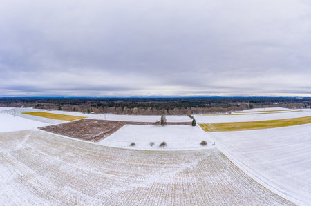 Wide winter aerial view over snowy fields with trees and a cloudy horizon, shot by a drone.の写真素材