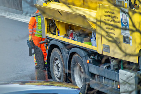 Maintenance at a manhole with a unrecognizable man, working behind the sewer cleaning vehicle on the...