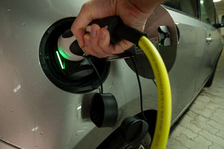 Hands on the charging wire of an e-car with an active charging process, shown by the green light.の写真素材